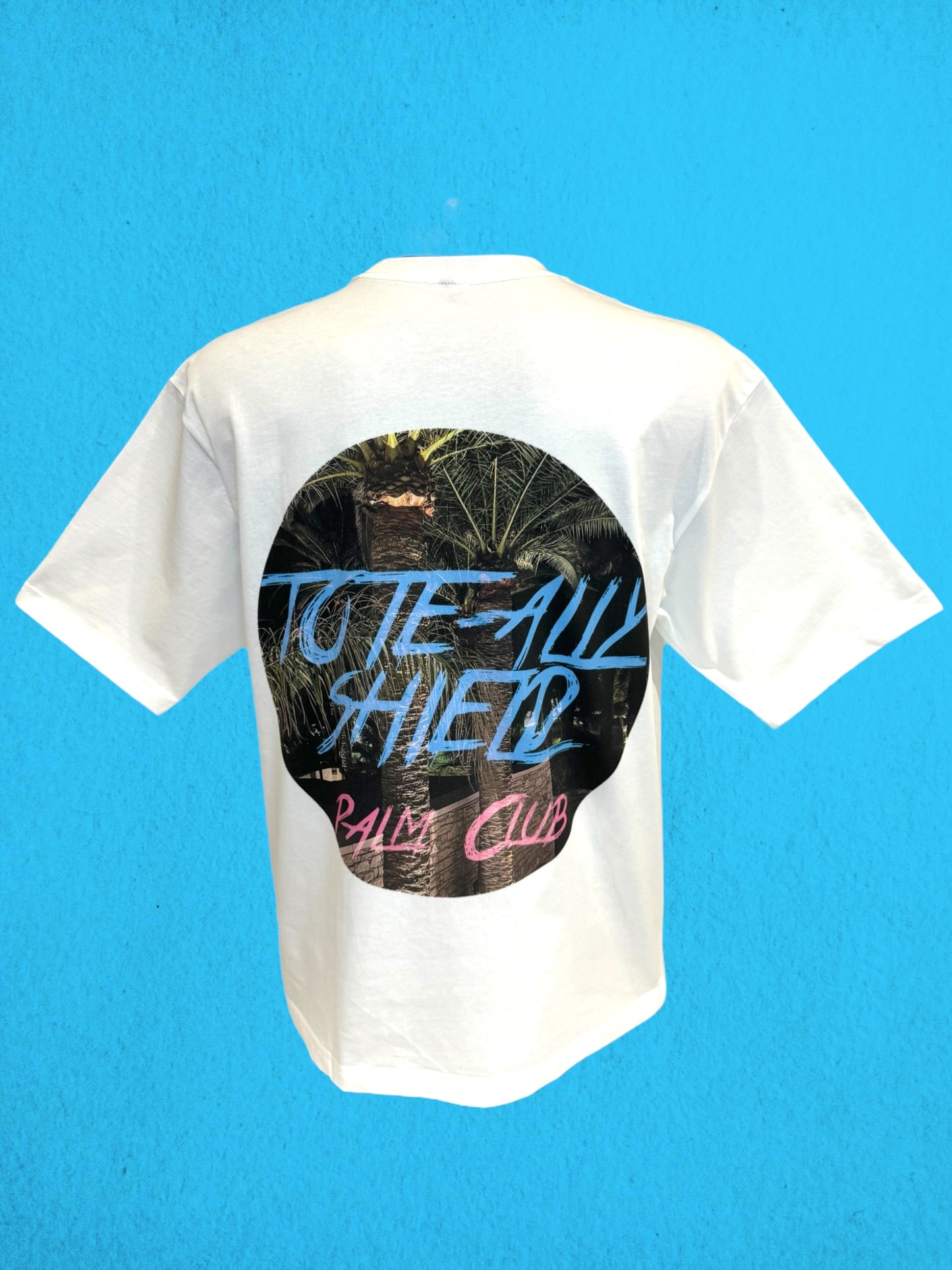 Back view of white short-sleeved, boxy-fit, heavyweight T-shirt featuring a large center-back graphic print. The ‘PALM CLUB’ design showcases a summer palm tree escape in a circular shape, with baby blue text highlighting the ‘TOTE-ALLY SHIELD’ logo and hot pink text highlighting 'PALM CLUB'.